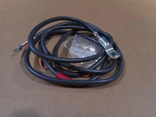 Kabel mit einem angeschlossenen Metallring und zwei abisolierten Leitungen. Verpackung mit kleinen Metallteilen im Hintergrund. Produkt von Remeha.